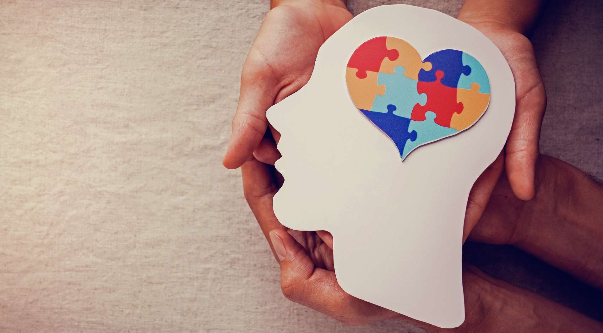 Image of hands holding a cutout of a head with a heart for a brain made of puzzle pieces