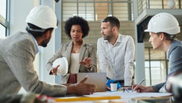Group of diverse project managers communicating while working on blueprints at construction building.