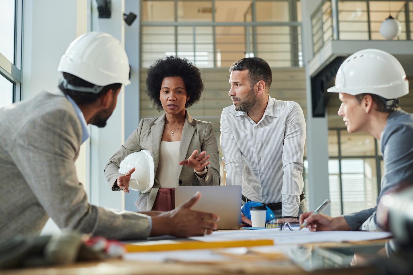 Group of diverse project managers communicating while working on blueprints at construction building.