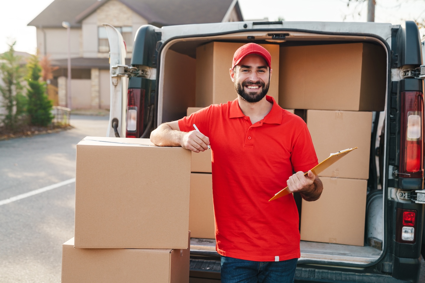 Image of delivery man holding clipboard while standing with boxes