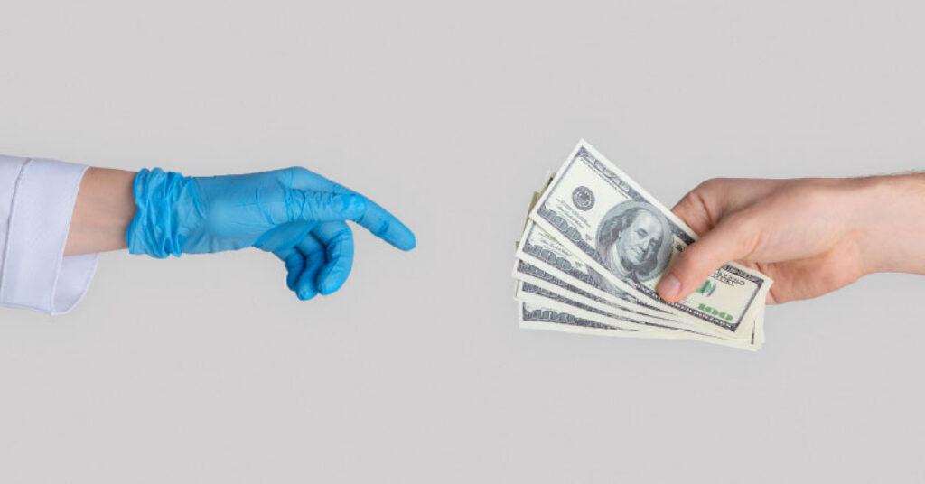 Close up of one hand holding cash handing it over to another medical professionals hand wrapped in a glove.