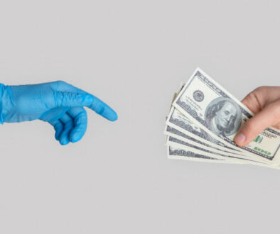 Close up of one hand holding cash handing it over to another medical professionals hand wrapped in a glove.