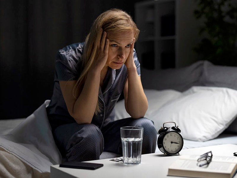 30_CarbonNews_SleepLarger Woman by her bed side with her head in her hands