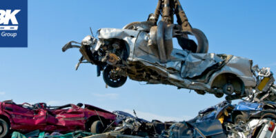 Crane holding demolished car in the air among field of wrecked cars