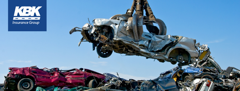 Crane holding demolished car in the air among field of wrecked cars